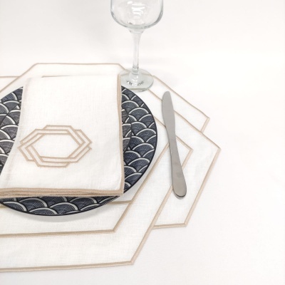 Mesa posta com jogo americano e guardanapo branco bordado, prato azul e copo de vidro