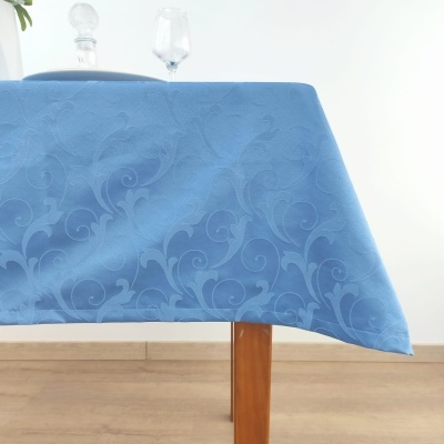 Toalha de mesa azul com padrão floral, mesa de madeira clara, garrafa e copo de vidro no fundo