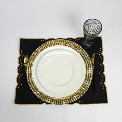 Conjunto de jantar com prato branco e dourado, talheres dourados e copo padrão geométrico em base preta com detalhes dourados