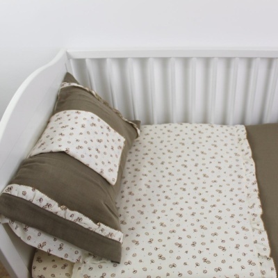 Berço branco com surrado e roupa de cama bege claro com padrão floral marron