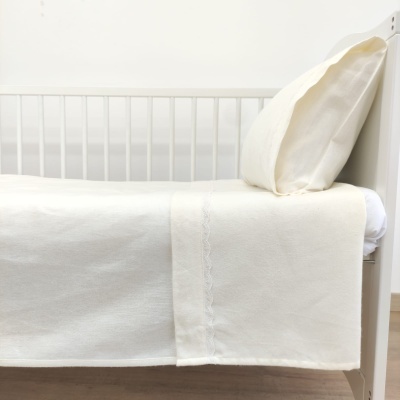 Berço branco com lençol e almofada creme claro com padrão relevo