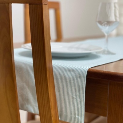 Mesa de madeira com toalha azul clara riscada, prato branco, copo de vidro e cadeiras de madeira