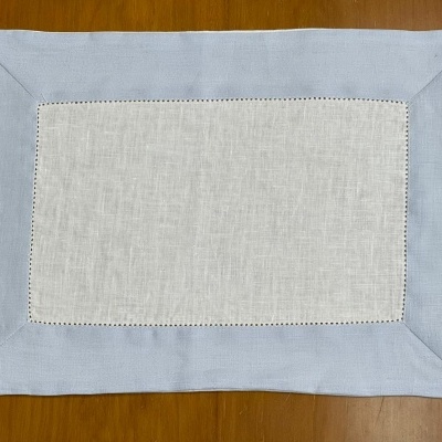 Toalhete retangular azul com centro branco e detalhes perfurados sobre mesa de madeira