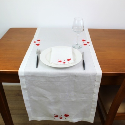 Caminho de mesa branco com bordado de corações vermelhos numa mesa de madeira com prato, guardanapo, talheres e copo