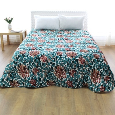 Colcha floral colorida em cama com almofadas brancas e mesa lateral com vaso de flores