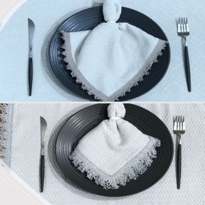 Prato preto com guardanapo branco bordado, talheres com cabos pretos sobre toalha branca bordada