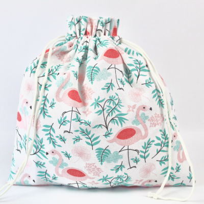 Saco de tecido branco com padrão de flamingos cor-de-rosa e folhas verdes.