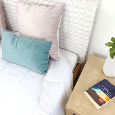 Cama com almofadas azul e rosa, edredão branco e mesa de cabeceira com livro
