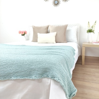 Cama branca com manta azul clara e almofadas bege e branco em quarto minimalista