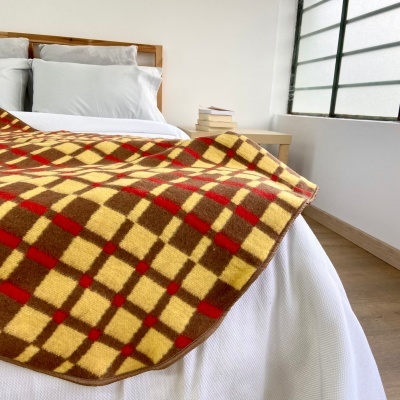 Cobertor quadriculado amarelo, castanho e vermelho sobre cama branca num quarto iluminado