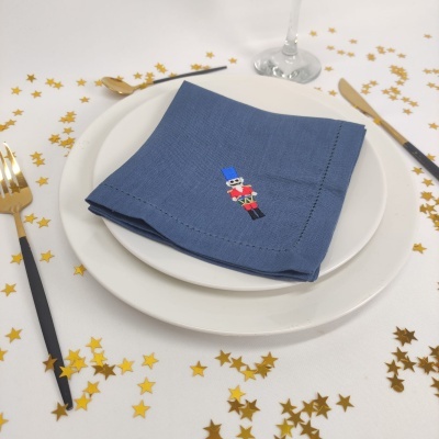 Guardanapo azul bordado com soldado de brinquedo sobre pratos brancos, talheres dourados e pretos, e confetes estrela dourados
