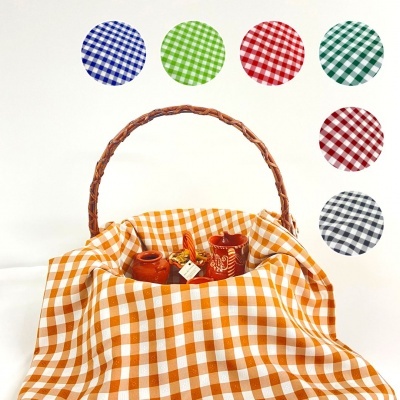 Pano de mesa xadrez vichy em várias cores numa cesta de verga com garrafas pequenas dentro