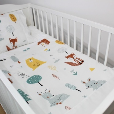 Berço branco com roupa de cama infantil estampada com animais e elementos naturais