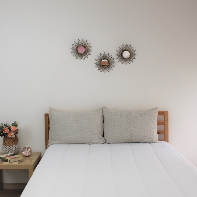 Cama branca com almofadas cinzentas e três espelhos decorativos na parede branca