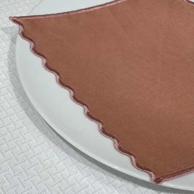 Guardanapo cor de ferrugem com borda rosa sobre prato branco e superfície texturada branca