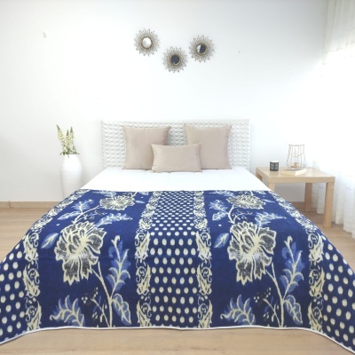 Colcha ou manta azul com padrão floral bege numa cama branca com almofadas bege num quarto minimalista