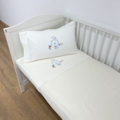 Cama de bebé branca com roupa de cama branca e bordados de ursinho azul