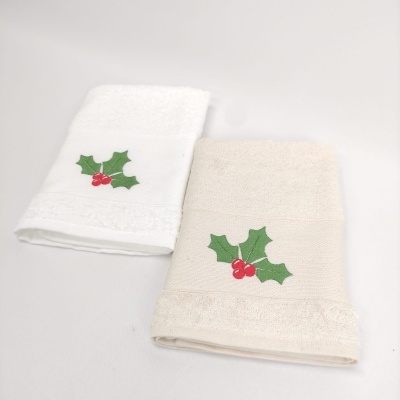 Duas toalhas pequenas bordadas com ramos de azevinho em verde e vermelho, uma branca e outra creme.