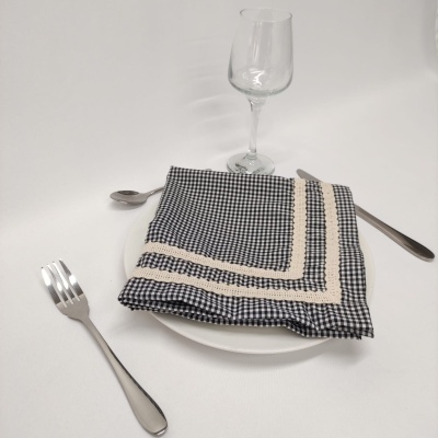 Mesa posta com guardanapo de tecido xadrez preto e branco, prato branco, talheres de metal e taça de vidro