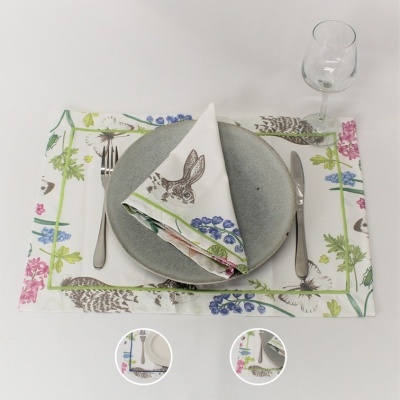 Conjunto de mesa com prato cinzento, guardanapo com coelho e padrão floral, talheres e copo de vidro