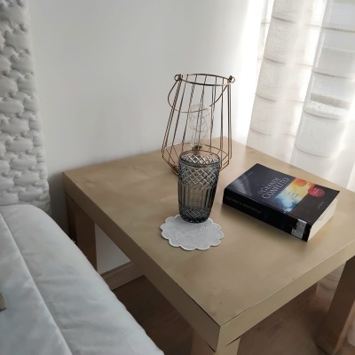 Mesa de cabeceira com candeeiro metálico, copo cinzento e livro O Caçador de Pipas