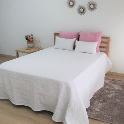 Cama com colcha branca, almofadas rosas e brancas, mesa de cabeceira e decoração