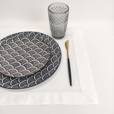 Conjunto de pratos com padrão de ondas, copo de vidro e faca com cabo preto sobre toalhete branco