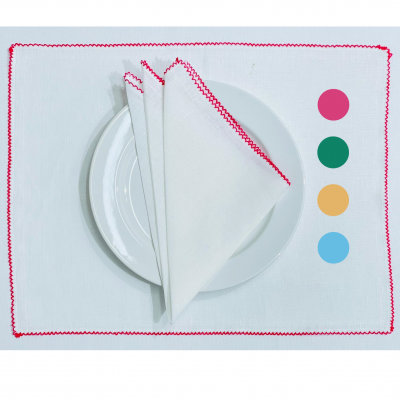 Jogo americano branco com borda vermelha e guardanapo a condizer sobre prato branco, cores circulares ao lado