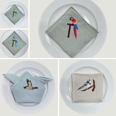 Guardanapos bordados com imagens de pássaros em pratos brancos