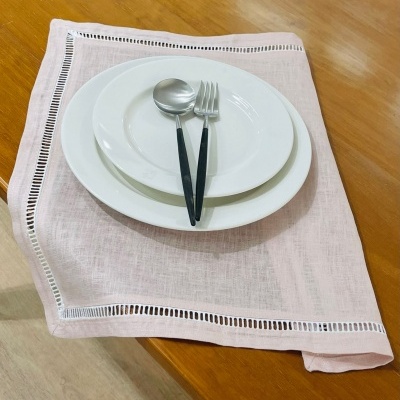 Conjunto de pratos brancos, talheres de metal com cabos pretos sobre pano de mesa rosa claro numa mesa de madeira.