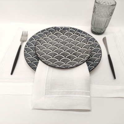 Conjunto de pratos com padrão de ondas, talheres com cabos pretos, guardanapo branco e copo de vidro transparente sobre toalha branca.