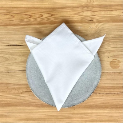 Guardanapo branco dobrado sobre prato cinzento numa mesa de madeira