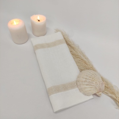 Toalha branca com riscas bege, velas acesas, concha e penugem decorativa sobre fundo branco