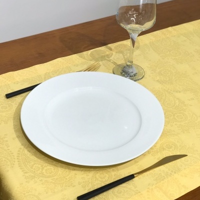 Prato branco, talheres com cabos pretos e taça com vinho branco sobre toalha amarela com padrões.