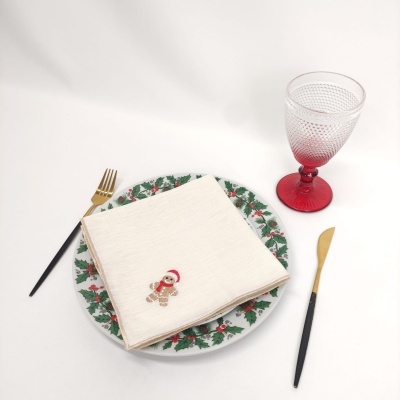 Conjunto de jantar com prato decorado, guardanapo com boneco de gengibre, talheres preto e dourado, copo vermelho texturizado.