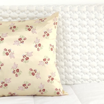 Almofada bege com padrão de flores vermelhas e lilases sobre cama branca texturizada.