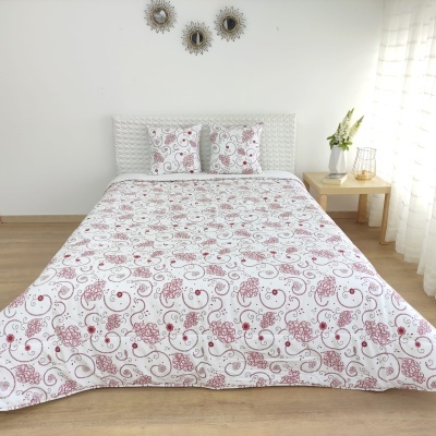 Colcha e almofadas com padrão floral vermelho e cinzento numa cama em quarto claro e minimalista