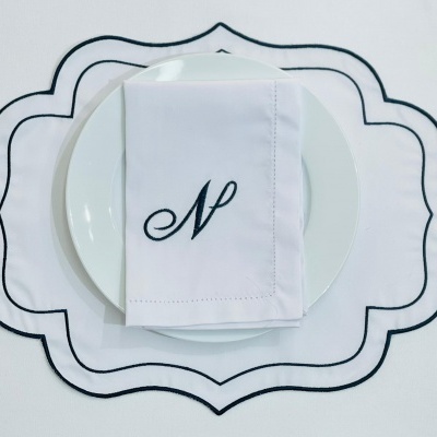 Guardanapo branco com letra N bordada em prato branco sobre lugar americano branco com bordas pretas