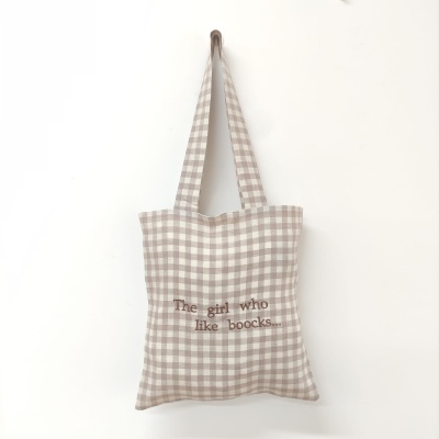 Saco de tecido xadrez bege e branco com texto bordado pendurado na parede