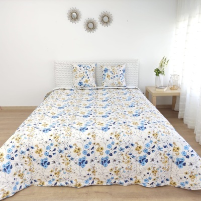 Colcha de cama floral azul e amarelo com duas almofadas, em quarto minimalista branco