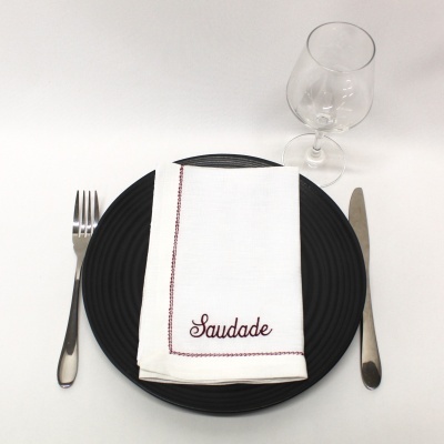 Conjunto de mesa com garfo, faca, prato preto, guardanapo branco com bordado e copo de vidro