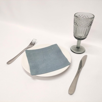 Talheres metal prateado, prato branco com guardanapo azul e copo cinza de vidro texturizado