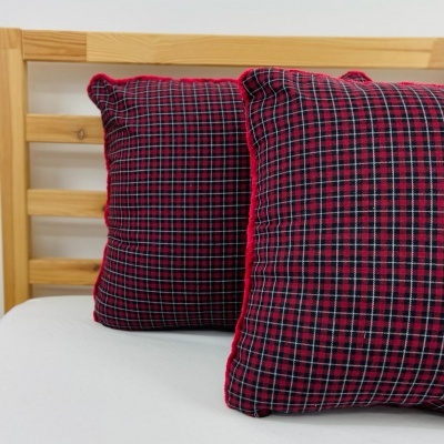 Duas almofadas xadrez vermelhas e azuis sobre cama com lençol branco e cabeceira de madeira
