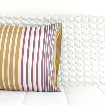 Almofada listrada colorida sobre cama branca texturada com pompons