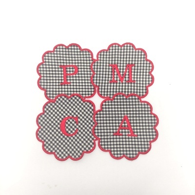 Quatro toalhetes com padrão xadrez preto, branco e cinzento, borda vermelha e letras vermelhas P, M, C, A no centro.