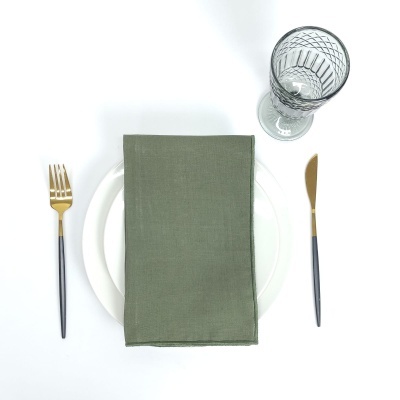 Conjunto para mesa com prato branco, guardanapo verde, talheres pretos e dourados e copo de vidro decorativo