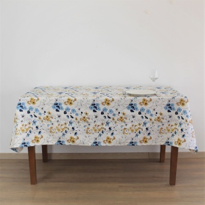 Mesa com toalha de mesa branca estampada com flores azuis e amarelas, prato e taça sobre a mesa