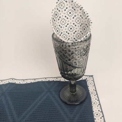Copo de vidro cinza com guardanapo branco estampado em tecido azul escuro.