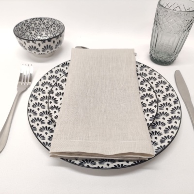 Prato e tigela brancos com padrão floral preto, guardanapo bege, talheres inox e copo de vidro com padrão geométrico