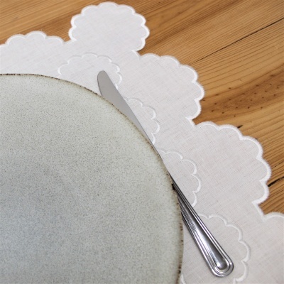 Prato cinzento com faca sobre centro de mesa branco bordado em mesa de madeira.